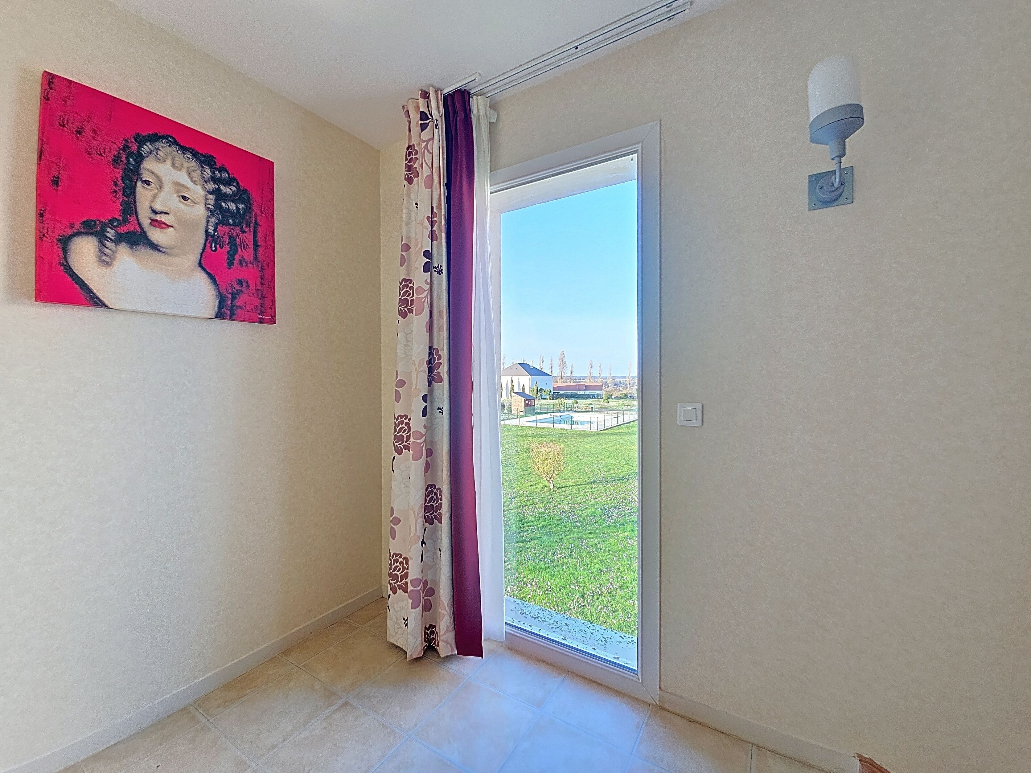 A room with a door leading to a balcony, a painting on the wall, and a security camera.