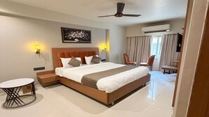Ein Hotelzimmer mit einem großen Bett, einem Schreibtisch, einem Sessel, einem Deckenventilator und einer Klimaanlage.
