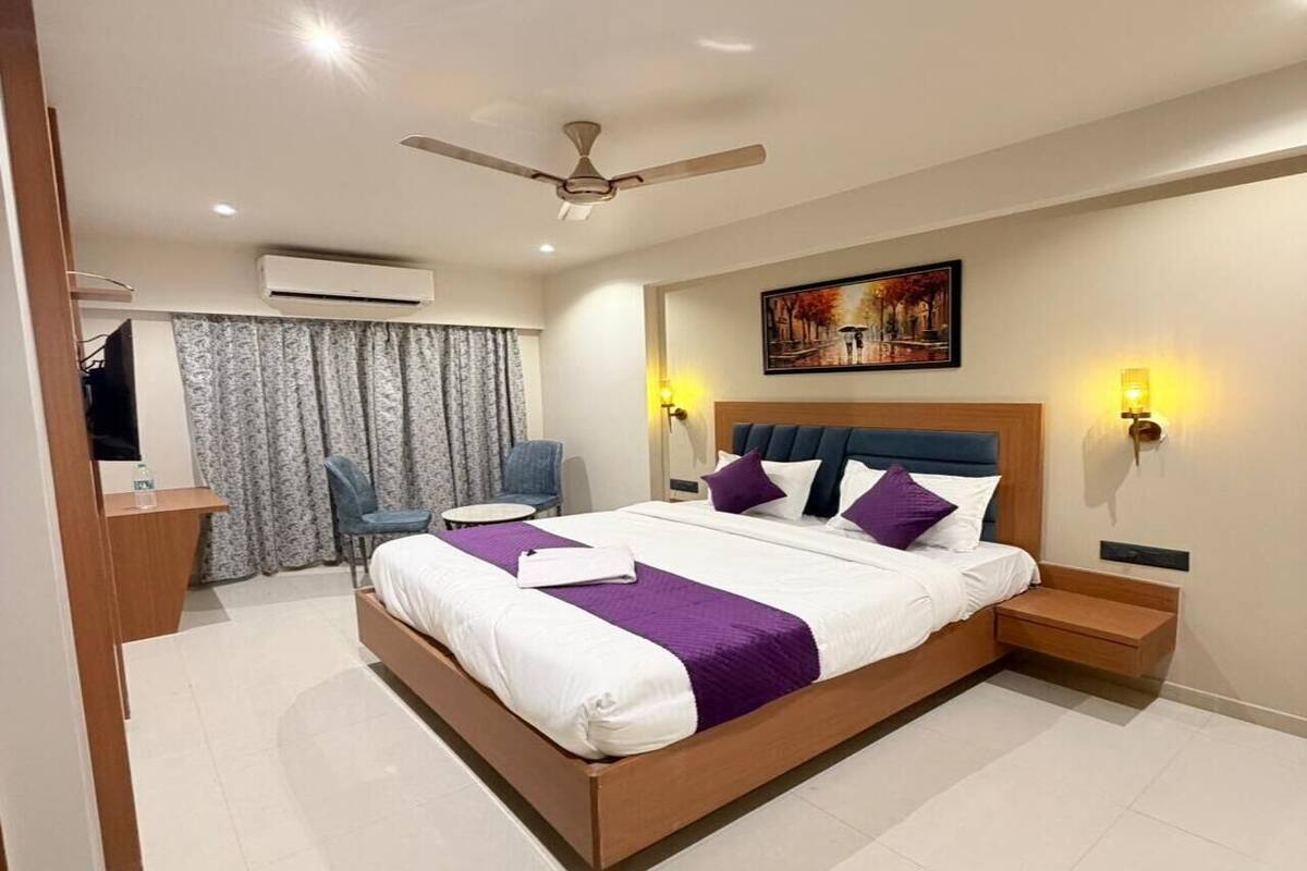 A modern hotel room with a large bed, a desk, a chair, a ceiling fan, and a painting on the wall.