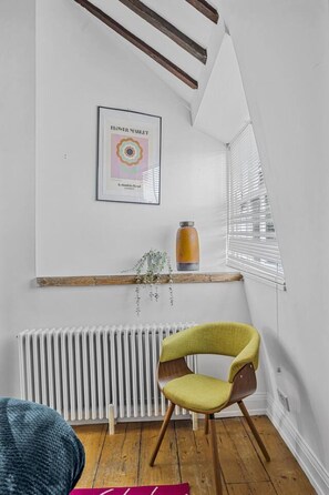 Ein Zimmer mit Heizkörper, einem gerahmten Bild an der Wand, einer Flasche und einem Sessel.