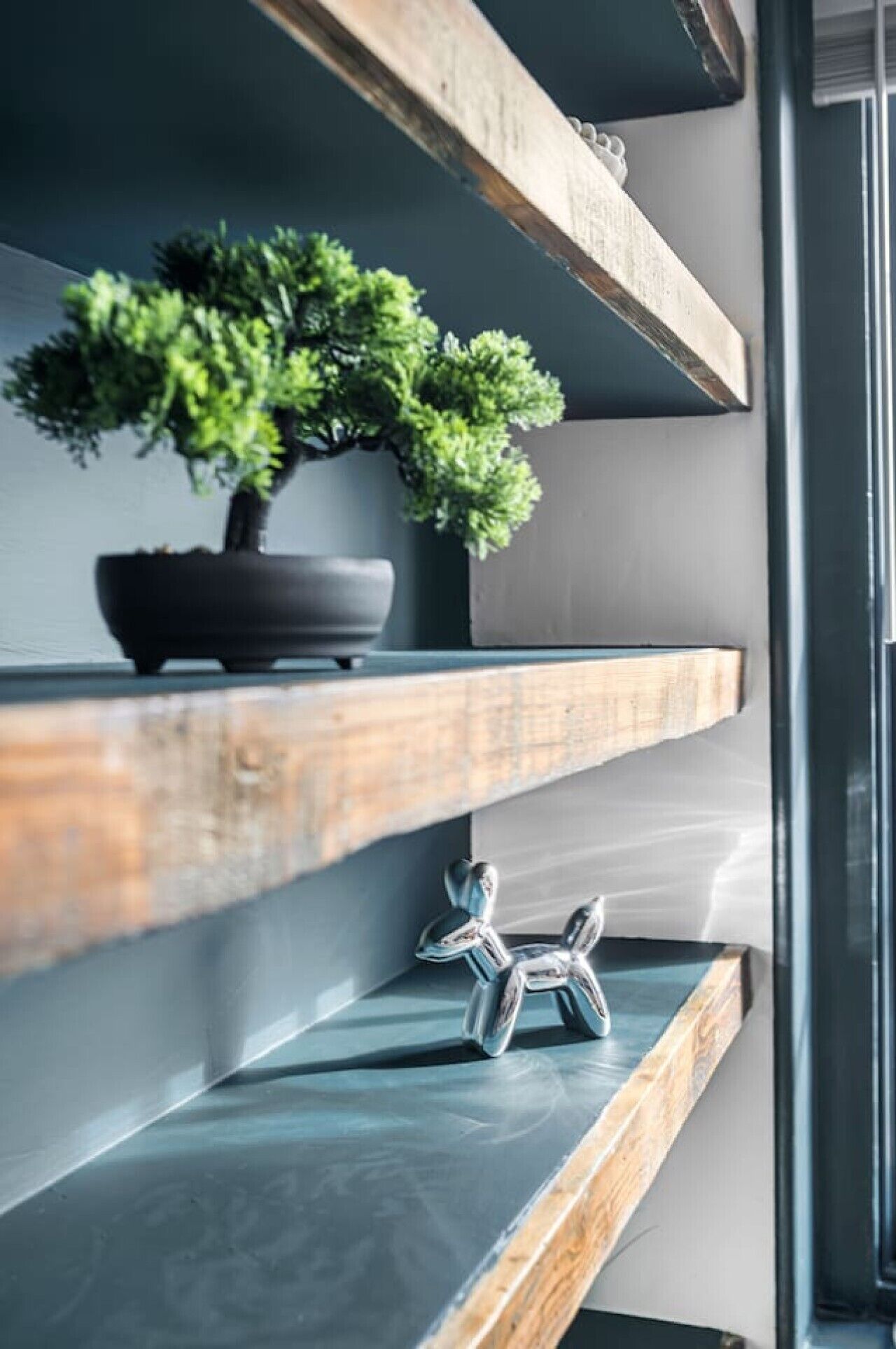 A modern interior with a potted plant on a wooden shelf, a metallic sculpture, and a glass door.