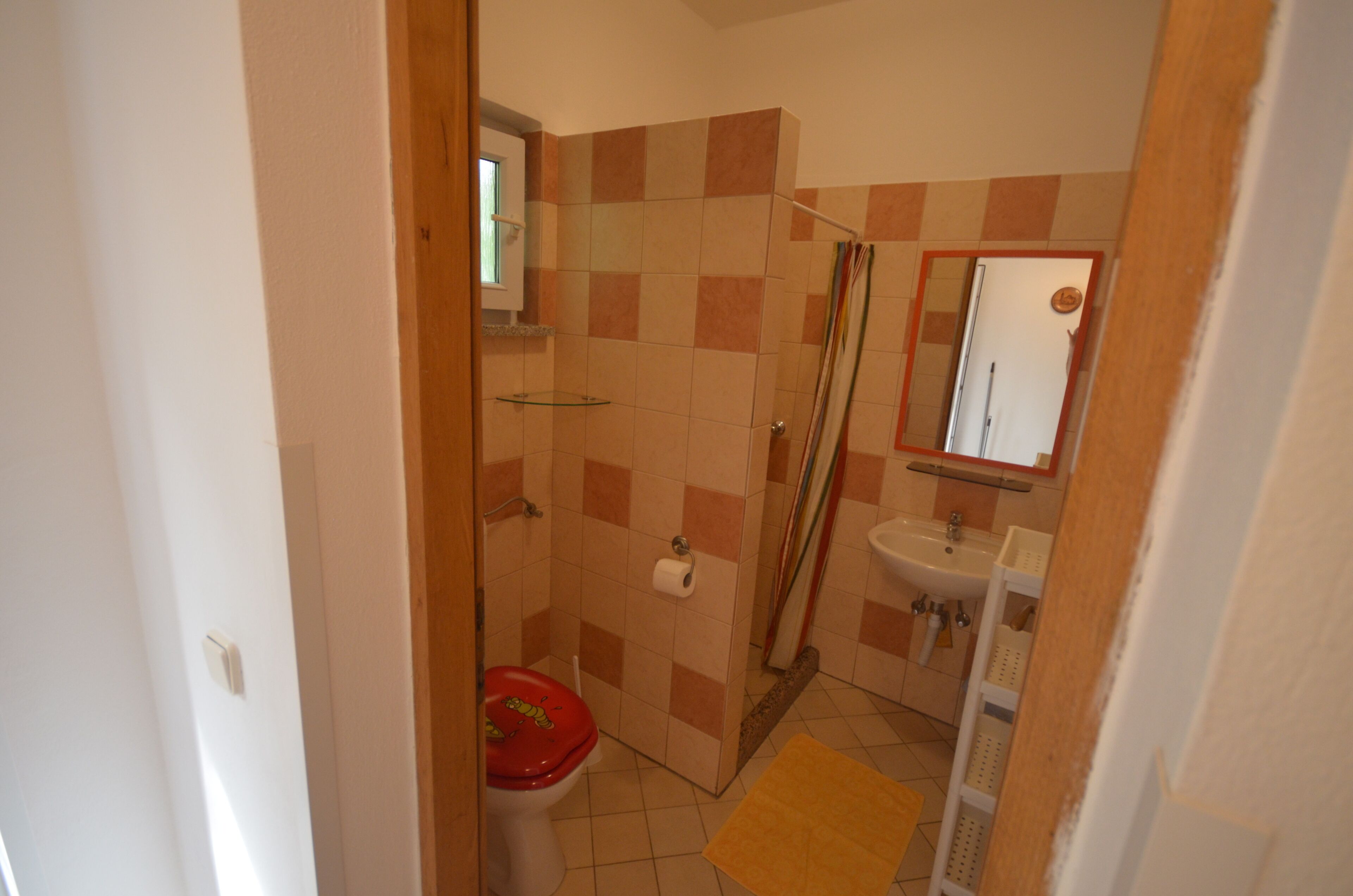 A bathroom with a toilet, shower, sink, and mirror.