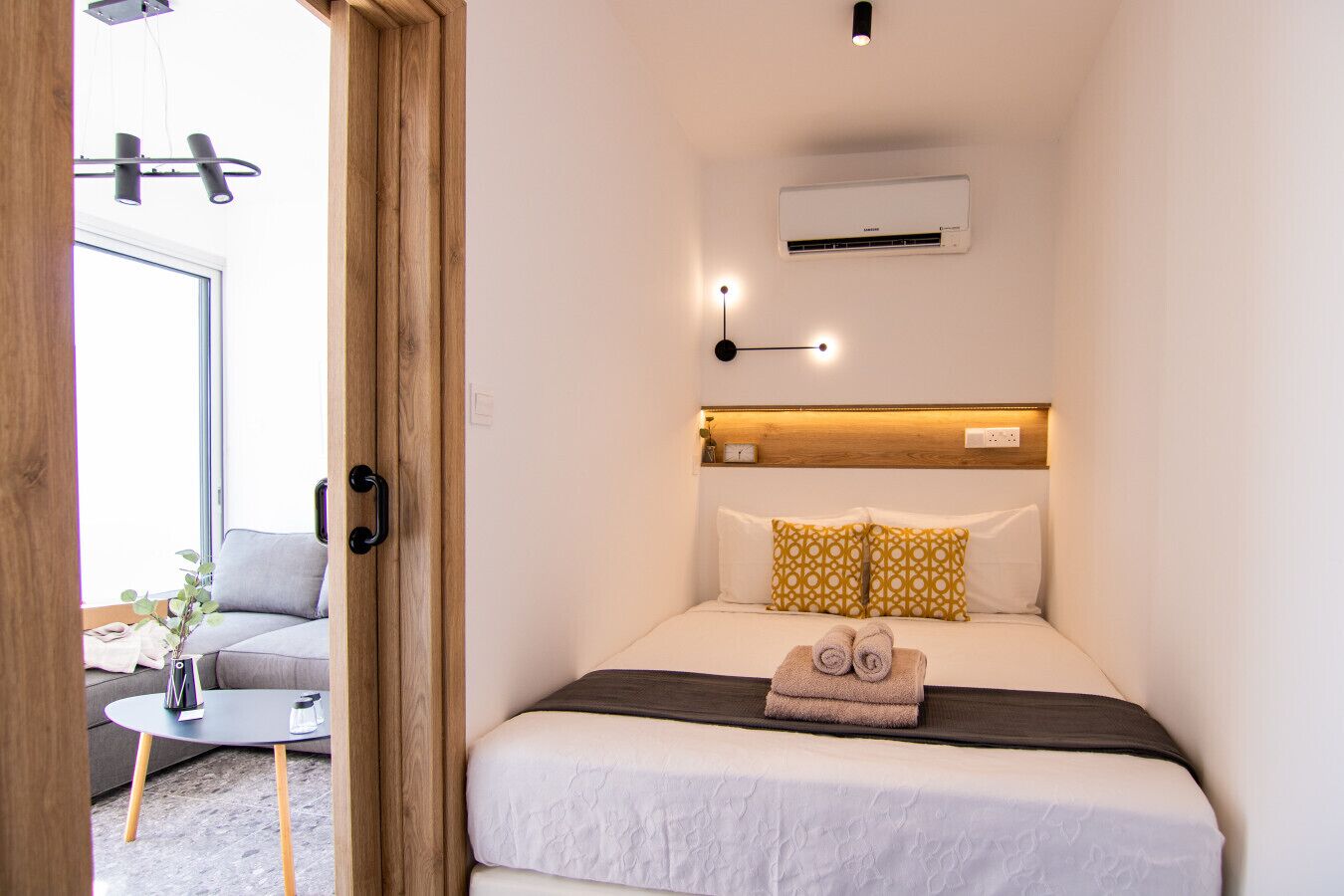 Une chambre d’hôtel compacte comprenant un lit, une table de chevet et un petit coin salon avec un canapé et une table.