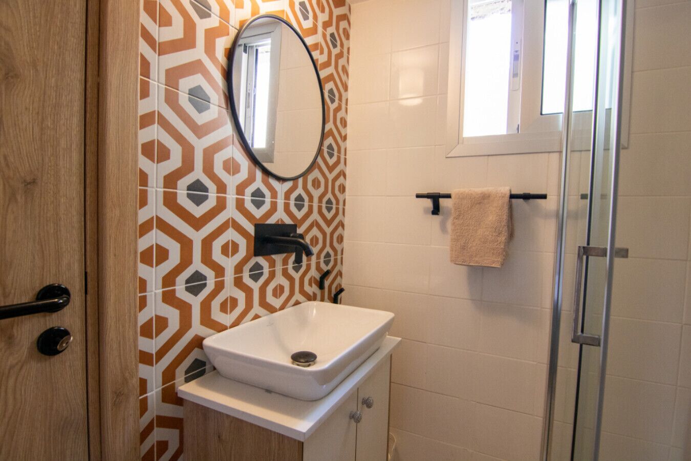 Une salle de bain avec un mur recouvert de carreaux à motifs, un lavabo blanc avec un robinet noir, un miroir et un porte-serviettes.