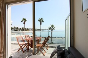 Ein Balkon mit Tisch, Stühlen, einer Couch und Blick auf das Meer und Palmen.