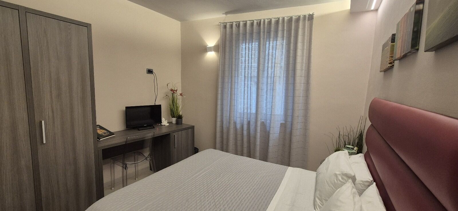 Een slaapkamer met een bed, een bureau met een televisie, een kledingkast en een raam met gordijnen.