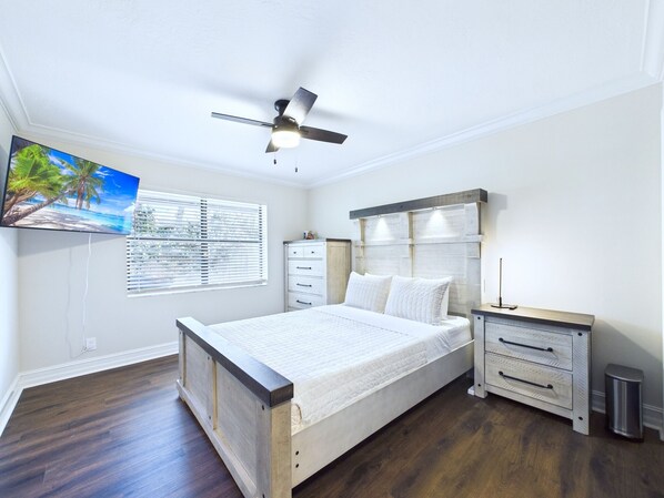A bedroom with a bed, a nightstand, a dresser, a ceiling fan, a TV, and a window with blinds. - This beautifully furnished 3-bedroom, 2-bath pool home offers bright open living spaces, a private backyard oasis, and the perfect setting for relaxing after a day at the beach. Ideal retreat for families, couples, and beach lovers alike. (Indian Harbor Beach)