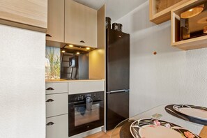 Una cocina compacta con horno integrado, refrigerador y un pequeño comedor con mesa redonda.