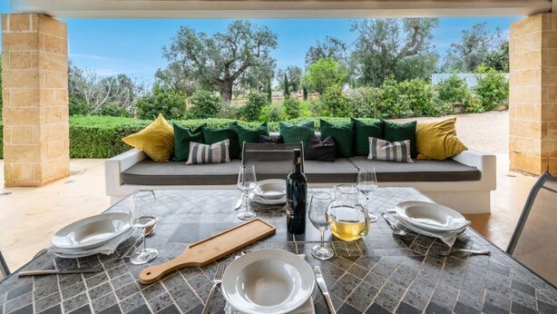An outdoor dining area with a table set for four, a bottle of wine, and a pitcher of water. - The Ridge House with Sea View by Rentbeat  (Carovigno)