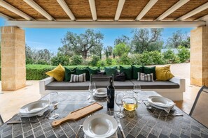 Un espace de restauration en plein air avec une table dressée pour quatre personnes, une bouteille de vin et une carafe d’eau.