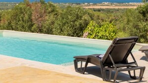 A pool with a lounge chair, surrounded by greenery and a view of the sea. - The Ridge House with Sea View by Rentbeat  (Carovigno)
