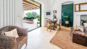 A room with a wicker sofa, a dining table with chairs, a green door, and a fireplace. - The Ridge House with Sea View by Rentbeat  (Carovigno)