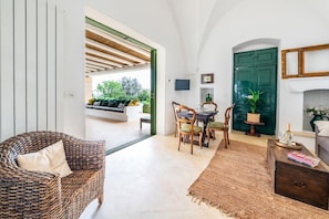 A room with a wicker sofa, a dining table with chairs, a green door, and a fireplace. - The Ridge House with Sea View by Rentbeat  (Carovigno)