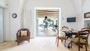 A room with a dining table set for four, a wicker chair, a television, and a view of an outdoor patio with a table and chairs. - The Ridge House with Sea View by Rentbeat  (Carovigno)