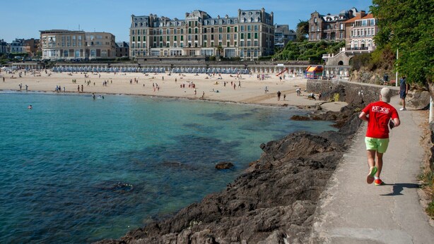 A coastal beach with a stone pathway leading to the water, a person jogging, and historic buildings in the background. - Accommodation for 4, 500m from the beach (Dinard)