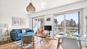 A modern living room with a blue sofa, wicker chairs, a glass dining table, and a large window with a view of buildings. - Accommodation for 4, 500m from the beach (Dinard)