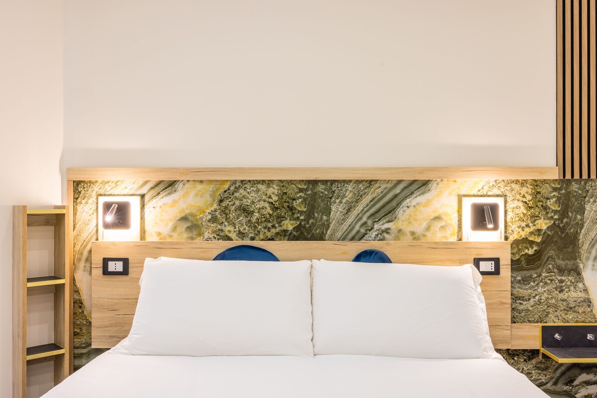 A bed with white bedding, a wooden headboard, and a wall with a marble-like pattern.