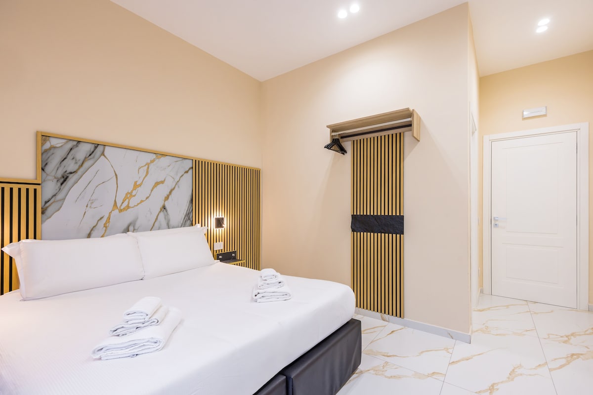 A hotel room with a bed, a marble wall art piece, a wall-mounted air conditioning unit, and a door.