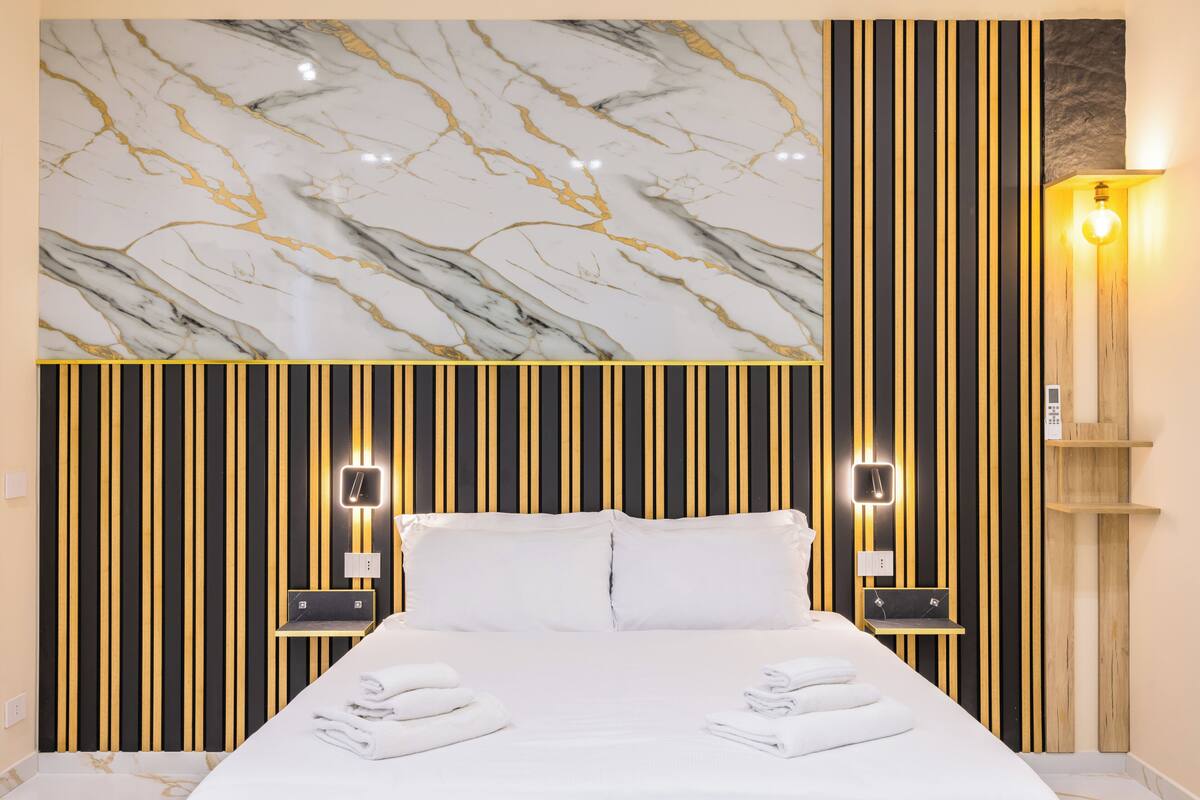 Ett hotellrum med en säng, två sängbord, en vägg i marmor och en vertikalrandig vägg med vägglampor.