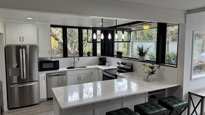 A modern kitchen with a central island, stainless steel appliances, and black bar stools.