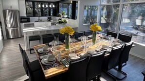 A modern kitchen with stainless steel appliances, a dining area with a wooden table set for six, and large windows offering a view of the outdoors.