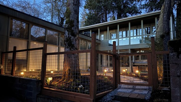 A modern house with large windows, a wooden fence, and a stone pathway.