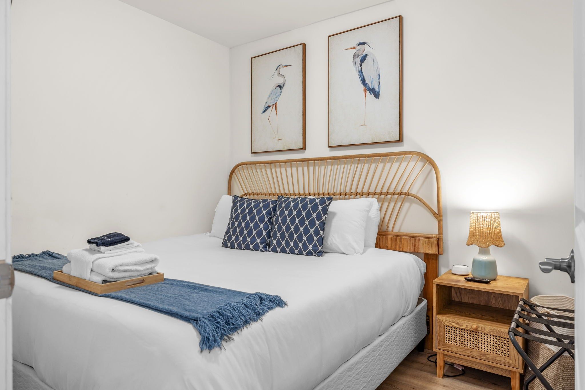 A neatly made bed with a white comforter and blue patterned pillows, a bedside table with a lamp, and two framed wall art pieces above the bed.