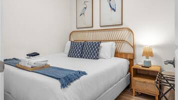A neatly made bed with a white comforter and blue patterned pillows, a bedside table with a lamp, and two framed wall art pieces above the bed.
