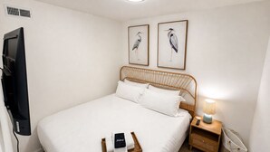 Una camera d'albergo con un letto, una televisione, un comodino con una lampada e due quadri appesi al muro.