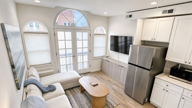 Una cucina moderna con mobili bianchi, un frigorifero in acciaio inossidabile e una TV a schermo piatto.