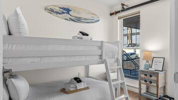 Un lit superposé avec une échelle, une table de chevet avec une lampe et une vue sur un parking à travers une porte vitrée.