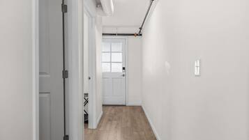Un couloir aux murs blancs, avec un plancher en bois et une porte au fond.
