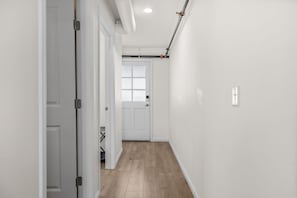 A hallway with white walls, a wooden floor, and a door at the end. - Salt & Serenity | Main Street & Free Parking (Saint Charles)
