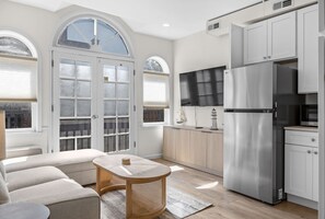 Open living area with sectional seating, coffee table, kitchenette, refrigerator, and arched glass doors. - Salt & Serenity | Main Street & Free Parking (Saint Charles)