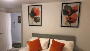 A hotel room with a bed, two pillows, a bedside table with a lamp, and two framed floral artworks on the wall. - Stylish Central Penthouse: Free Parking & Wi-Fi (Derby)