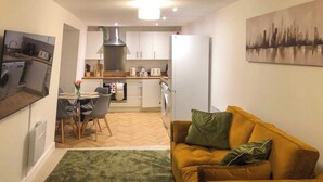 A compact living space with a sofa, a dining table with chairs, a kitchen area, and a mounted television. - Stylish Central Penthouse: Free Parking & Wi-Fi (Derby)