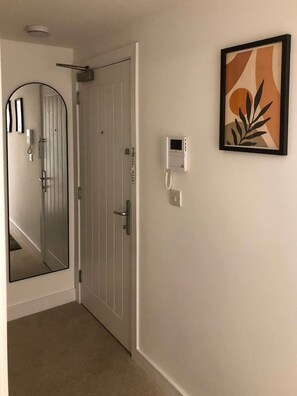 A hallway with a white door, a mirror, a framed artwork, and a thermostat on the wall. - Stylish City Centre Penthouse w/ Free Parking (Derby)