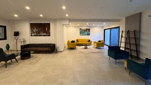 Ein geräumiges Wohnzimmer mit einer großen Couch, einem gelben Sessel und einem blauen Sessel. An der Wand hängt ein Gemälde und es steht eine Stehlampe da.