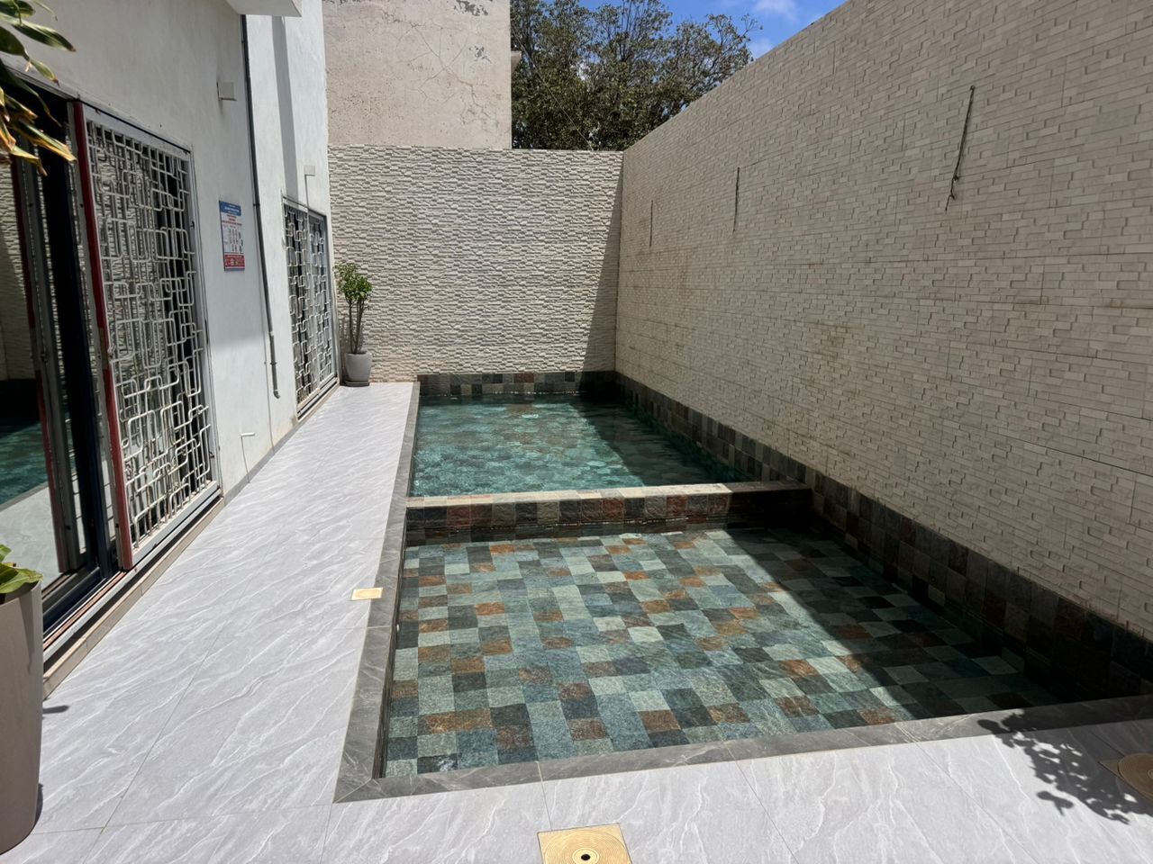 A courtyard with a pool, tiled floor, and a brick wall.