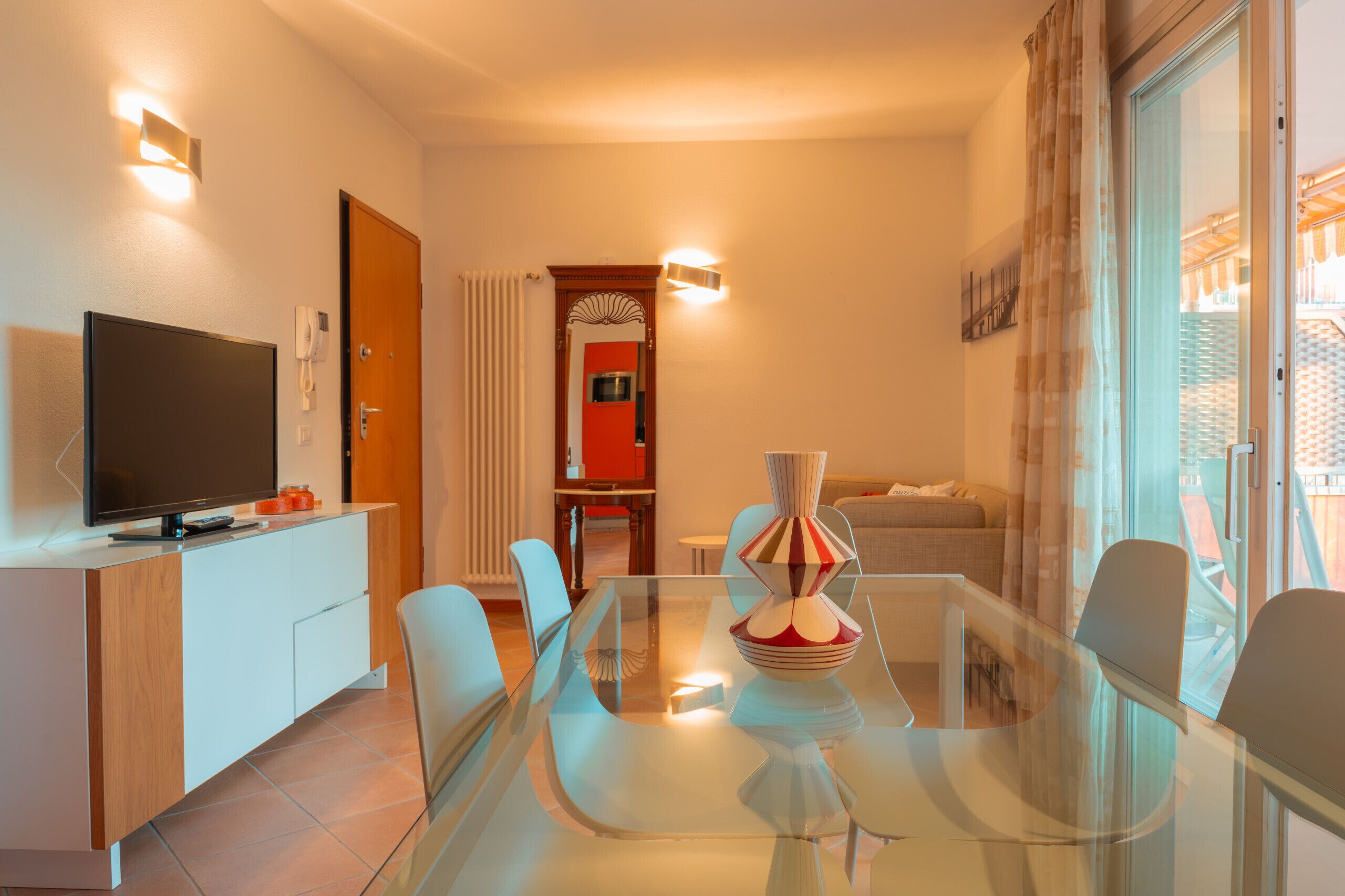 Habitación de hotel moderna con mesa de comedor de vidrio, televisor de pantalla plana, sofá y balcón con vistas.