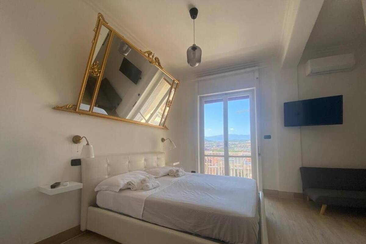 Un dormitorio con cama, un espejo grande, una mesita de noche, televisor y balcón con vistas.