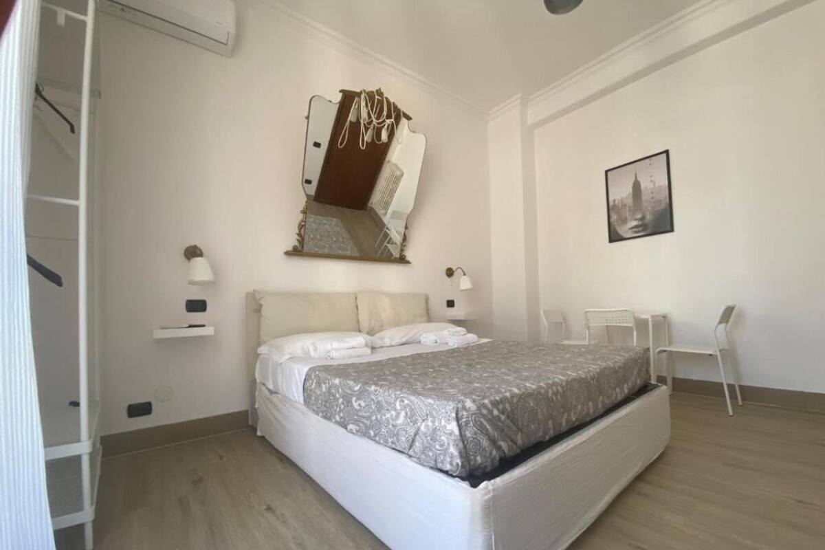 Un dormitorio con cama, una silla, un escritorio, un estante en la pared y un cuadro.