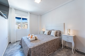 Ein Schlafzimmer mit Bett, Nachttischen, einem Fenster mit Vorhängen und Blick auf Gebäude.