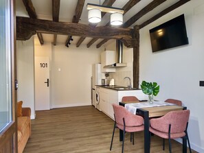 Een moderne keuken met houten balken, een eethoek met roze stoelen, en een aan de muur bevestigde televisie.