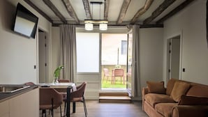 A modern living room with a sofa, a dining area with chairs, a TV mounted on the wall, and a view through a glass door to an outdoor area. - Casa De Postas - Bajo con jardín, 2 dormitorios (San Mamés de Meruelo)
