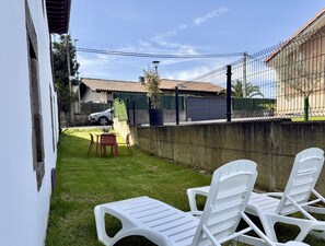 A backyard with a concrete wall, a small table with chairs, and a parked car. - Casa De Postas - Bajo con jardín, 2 dormitorios (San Mamés de Meruelo)