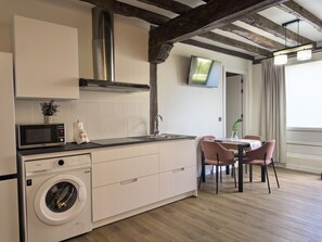 A compact kitchen with a washing machine, a microwave, and a dining area with chairs. - Casa De Postas - Bajo con jardín, 2 dormitorios (San Mamés de Meruelo)
