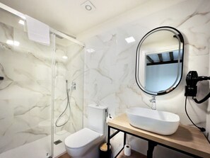 A bathroom with a marble wall, a toilet, a sink with a large mirror, and a handheld showerhead. - Casa De Postas - Bajo con jardín, 2 dormitorios (San Mamés de Meruelo)