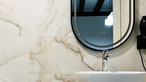 A bathroom with a white marble tile wall, a round mirror, a white sink, and a wooden countertop. - Casa De Postas - Bajo con jardín, 2 dormitorios (San Mamés de Meruelo)