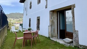 A white building with a patio area featuring a table and chairs, a view of the surrounding landscape, and a door leading to an interior space. - Casa De Postas - Bajo con jardín, 2 dormitorios (San Mamés de Meruelo)